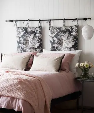 Un esempio di idee per la camera degli ospiti che mostra un letto con lenzuola e cuscini rosa e una testiera composta da cuscini sospesi