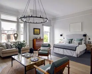 Una grande camera da letto con un letto bianco e un angolo salotto con sedie, tavolino e una grande plafoniera