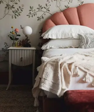 Un letto rosa con lenzuola bianche davanti a una carta da parati floreale