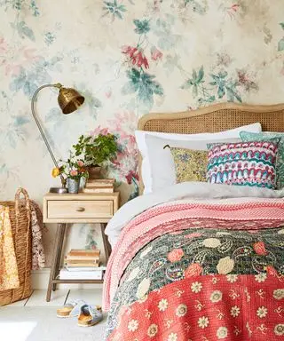 Un esempio di idee per la camera degli ospiti che mostra una camera da letto colorata con un letto con testiera in rattan davanti a una carta da parati floreale colorata