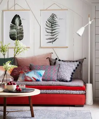 Un esempio di idee per la camera degli ospiti che mostra un divano letto rosso con cuscini davanti a un muro bianco con opere d'arte appese