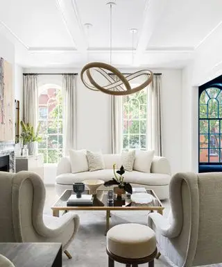 salon avec murs blancs et canapés blancs et fauteuils beiges avec de hautes fenêtres