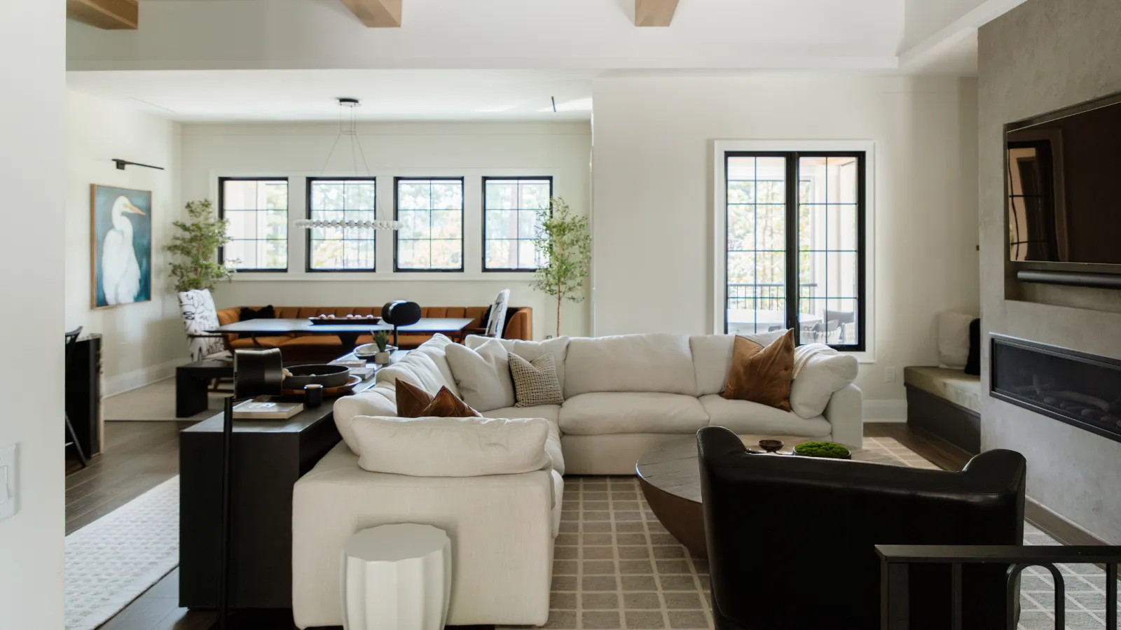 un invitante soggiorno con un grande divano componibile color crema, una poltrona in pelle, un tappeto a motivi geometrici, una consolle scura dietro il divano con decorazioni e una TV integrata nel muro sopra un caminetto' loading='lazy' title=