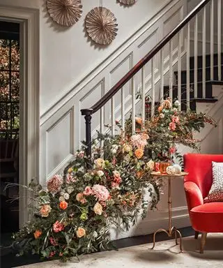 Juletrappdekorasjoner med et blomsterarrangement ved bunnen av rekkverket med vinterblomster i rosa, røde og oransje