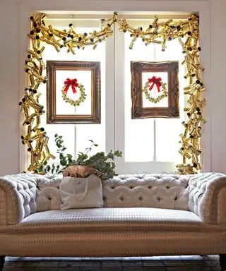 Weihnachtsdeko-Ideen für Fenster mit einer Girlande aus Goldknallbonbons und gerahmten Kränzen an jedem Fenster