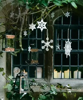 Ideen für die weihnachtliche Fensterdekoration mit weißen Dekorationen am Baum vor dem Fenster