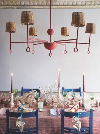 Mesa navideña con mesa puesta para la cena con velas encendidas, galletas navideñas, guirnaldas de honestidad, vajillas de colores brillantes, gran lámpara central arriba