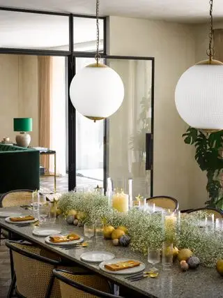 Comedor navideño con mesa dispuesta, guirnaldas de gypsophila, velas tipo huracán, adornos dorados y cubiertos