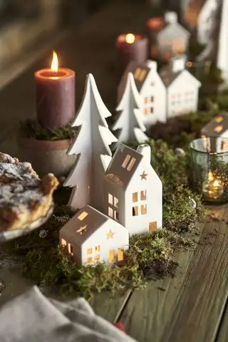 Mesa navideña con velas de té, musgo y guirnaldas de follaje.