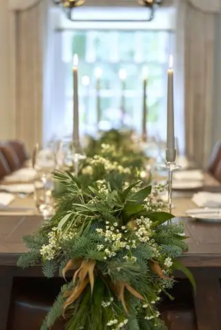 Guirnalda de mesa navideña con follaje, velas, vajilla.