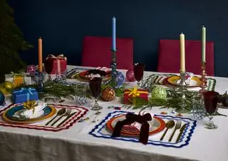 Mesa navideña con guirnaldas de follaje, adornos, manteles individuales, velas, regalos de mesa, árbol en la esquina
