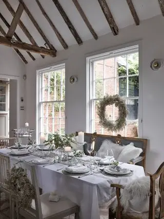 Comedor navideño blanco con ambientes festivos, guirnaldas de cuentas, coronas interiores, bancos y sillas de comedor