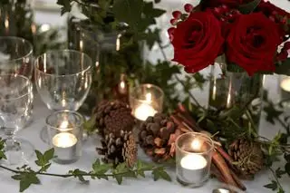 Mesa festiva con jarrones de rosas rojas y bayas, piñas, ramas de canela y guirnaldas de follaje.