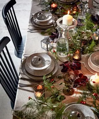 Mesa de comedor navideña decorada con follaje colorido, vajillas, adornos y velas.