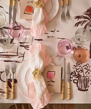 Cubierto de inspiración francesa para una cena de celebración, con servilleta con volantes y mantel pintado a mano