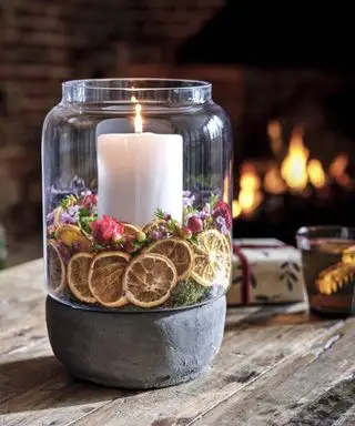 Kerzenaufsatz im Glasgefäß, umgeben von Orangenscheiben und Blumen