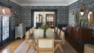 En spisestueidé med blå tapet med William Morris-trykk, stor mørk treskjenk og lyst tre spisebord med rottingstoler
