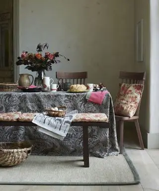 Høstbordsdekorasjoner med en gråmønstret duk, oransje og rosa sitteputer og oransje og rosa blomster
