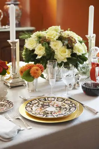 høstbord med kremroser og bær i vase, oransje dahlia, glass med gullkant, mønstrede tallerkener, sølvlysestaker