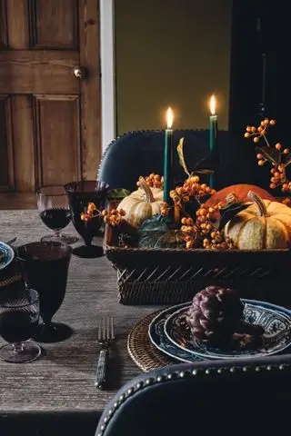 Halloween borddekor med kurv full av kalebasser, bær og grønne lys, blåmønstrede tallerkener med rotting dekkebrikker, bærfarget glass