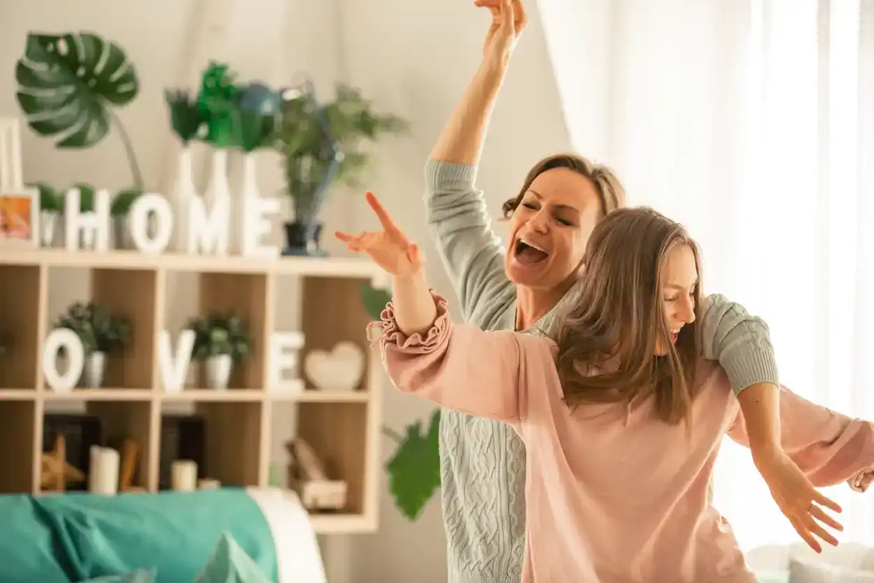 Mother and her daughter captured in the moment of pure joy and laughter while dancing and singing together in their living room.