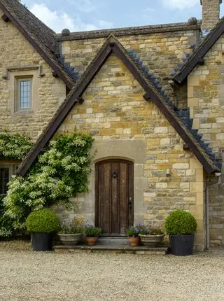 Exterior de la parte delantera de la cabaña de piedra de Cotswold con el camino de grava en primer plano