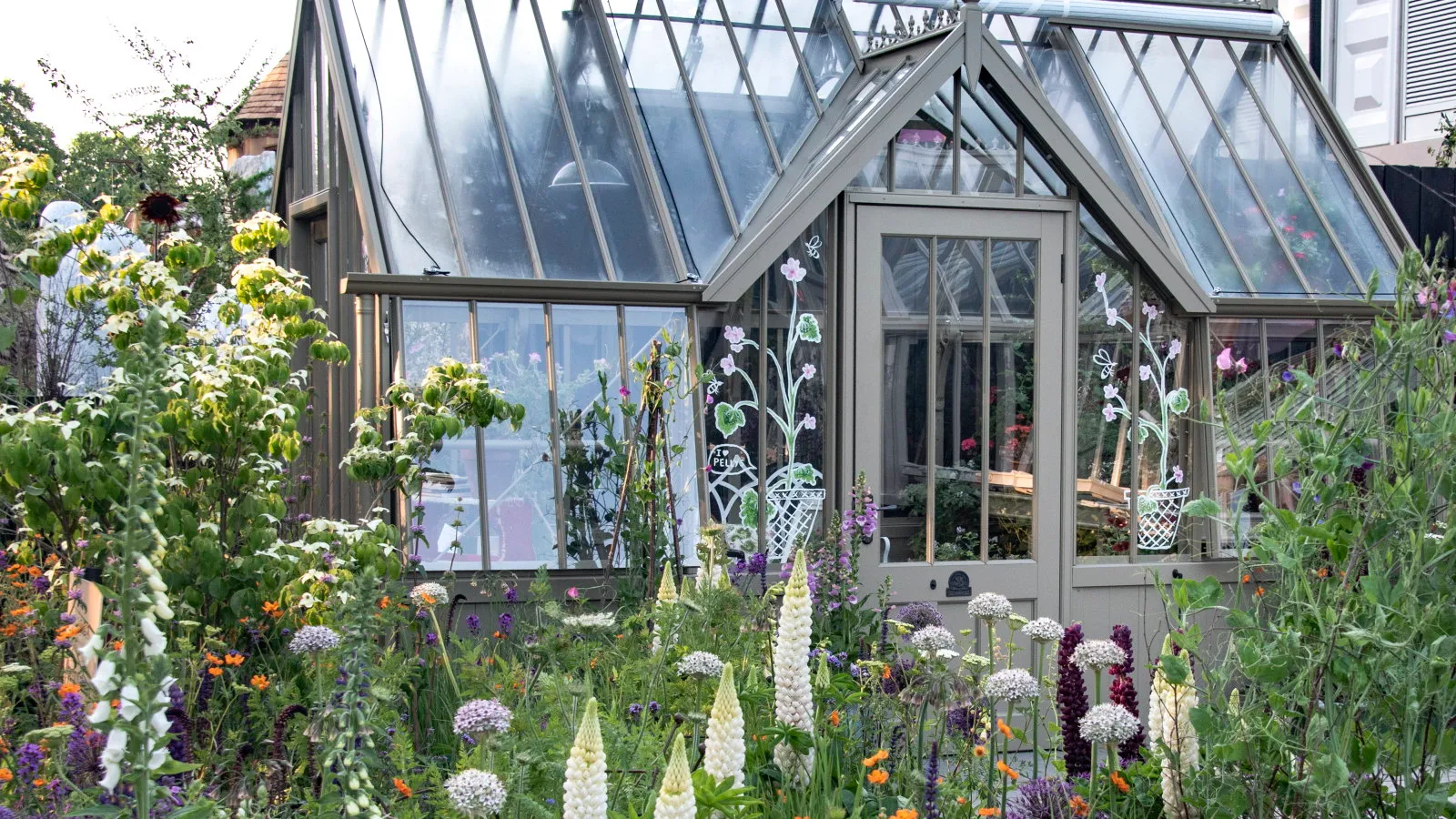 Et storslået drivhus omgivet af blomsterfyldte senge på Chelsea Flower Show' loading='lazy' title=