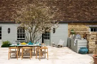 Área de cocina al aire libre con parrilla, mesa de comedor y sillas.