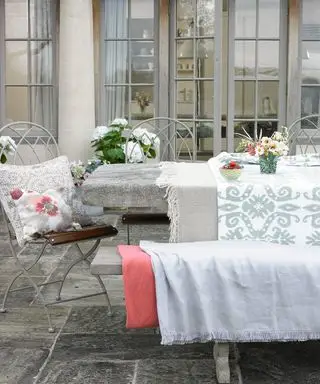 Et eksempel på udendørs spiseideer, der viser et spisebord på en terrasse med grå stole og tæpper i grå og pink nuancer