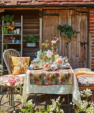 En udendørs spiseplads med et bord dekoreret med blomsterduge og stole med farverige hynder