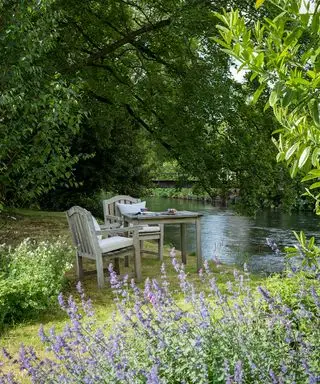 Et spisebord i træ med to stole ved siden af ​​en flod foran lavendel