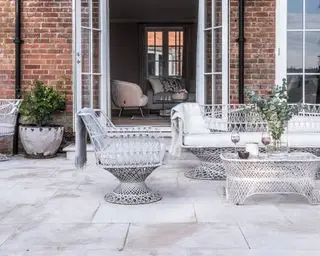 Hvor meget koster en gårdhave, illustreret med høje naturstensudlæggere foran et murstenshus med moderne havemøbler i hvidt metal.