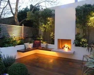 kleine Terrasse mit Holzterrasse, Außenkamin, Sitzgelegenheiten und Hochbeeten mit beleuchtetem Bambus