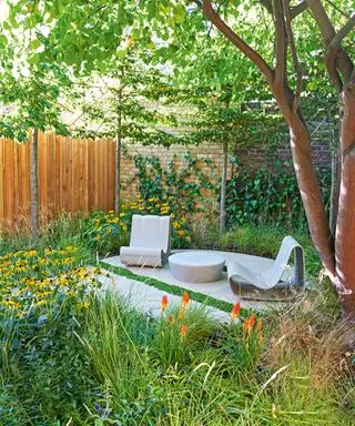 Gartentrends mit Gartenmöbeln, zwei geschwungenen Liegestühlen und Couchtisch auf runder Terrasse
