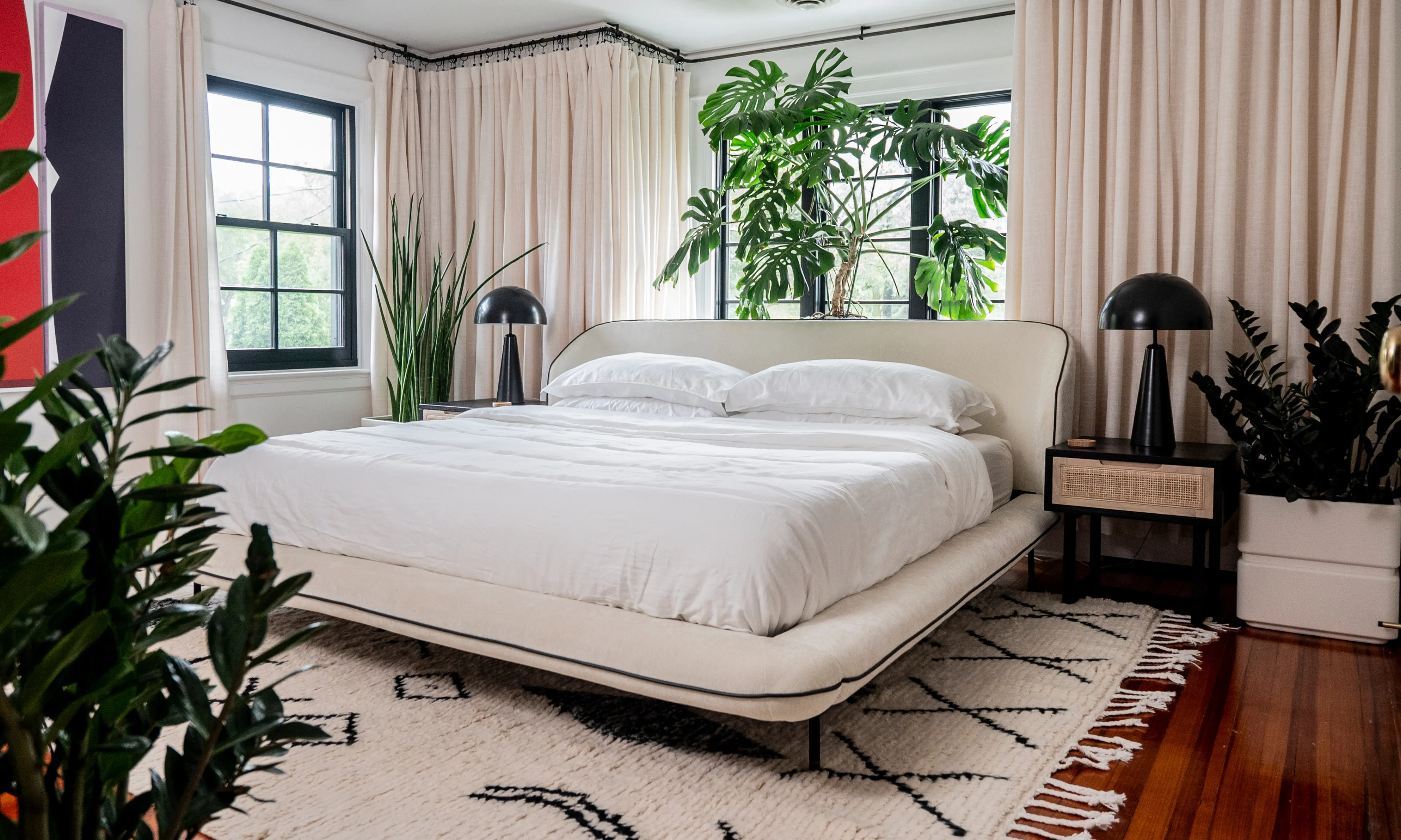 Grande planta monstera atrás de uma cama perto de uma grande janela em um quarto' loading='lazy' title=