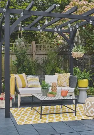Eine Terrasse und Pergola mit einem Sofa im Freien, einem Couchtisch auf einem gelben Teppich und Lichterketten