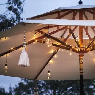 Ein Beispiel für Ideen für eine Außenbeleuchtung mit Lichterketten, das einen Gartensonnenschirm mit Lichterketten zeigt