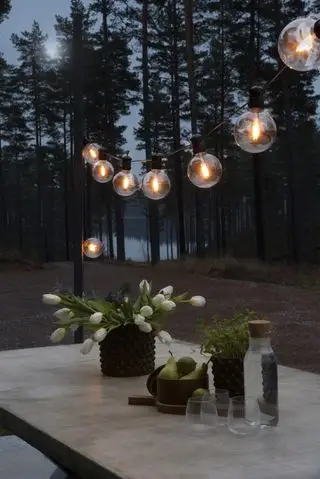 Ein Esstisch im Freien mit Glühbirnen-Lichterketten und einer Vase mit Tulpen