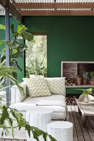 Una terraza de madera con una pared verde, muebles rústicos de exterior y un sofá color crema.