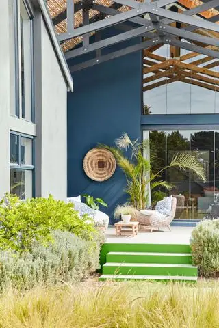Un ejemplo de ideas para un gran patio trasero que muestra una terraza colorida que conduce a un jardín con pastos y arbustos silvestres.