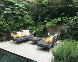 Pequeño patio con jardín con zona de estar en la terraza y plantas de hoja perenne.