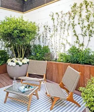 pequeño patio amurallado con jardineras de madera, asientos y alfombra