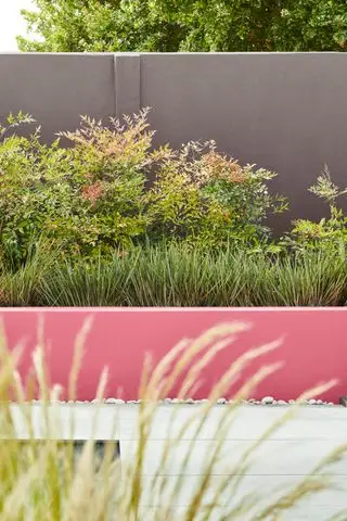 Sådan designer du en gårdhave med hårdt landskab, med en koralmalet betonvæg, der skaber et blomsterbed foran en højere grå væg.