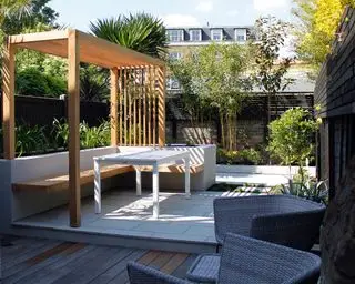 Design af en gårdhave med en pergola til ly, med indbyggede bænke i en skyggefuld byhave.
