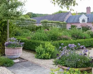 Sådan designer du en terrasse i en formel landhyttehave med grus, stenterrasse og store plantekrukker.