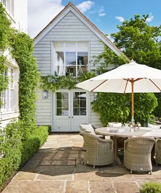Design af en terrasse i en lille landhave med bord, stole og hvid parasol.