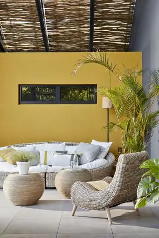 Design af en terrasse illustreret med gule og grå vægge og afrundet flet havesofa, stol og sofaborde.