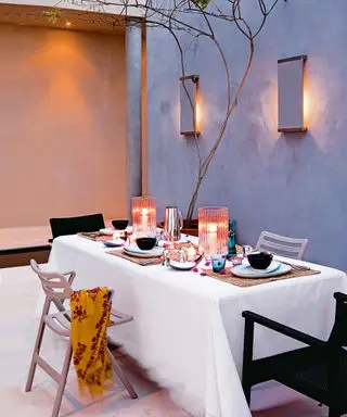 Terrasse mit Beleuchtung an der Wand und Kerzen auf einem zum Abendessen gedeckten Tisch