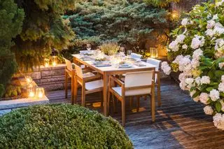 beleuchteter Terrassenbereich mit Holzmöbeln und Hecken