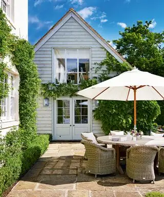 Ein geschwungener Holztisch und Korbstühle demonstrieren Ideen für Terrassenmöbel in einer kleinen Terrasse im Landhausstil mit Kletterpflanzen.